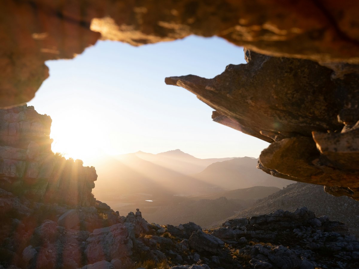 Blick aus einer Felsöffnung auf eine Berglandschaft bei Sonnenaufgang oder Sonnenuntergang.