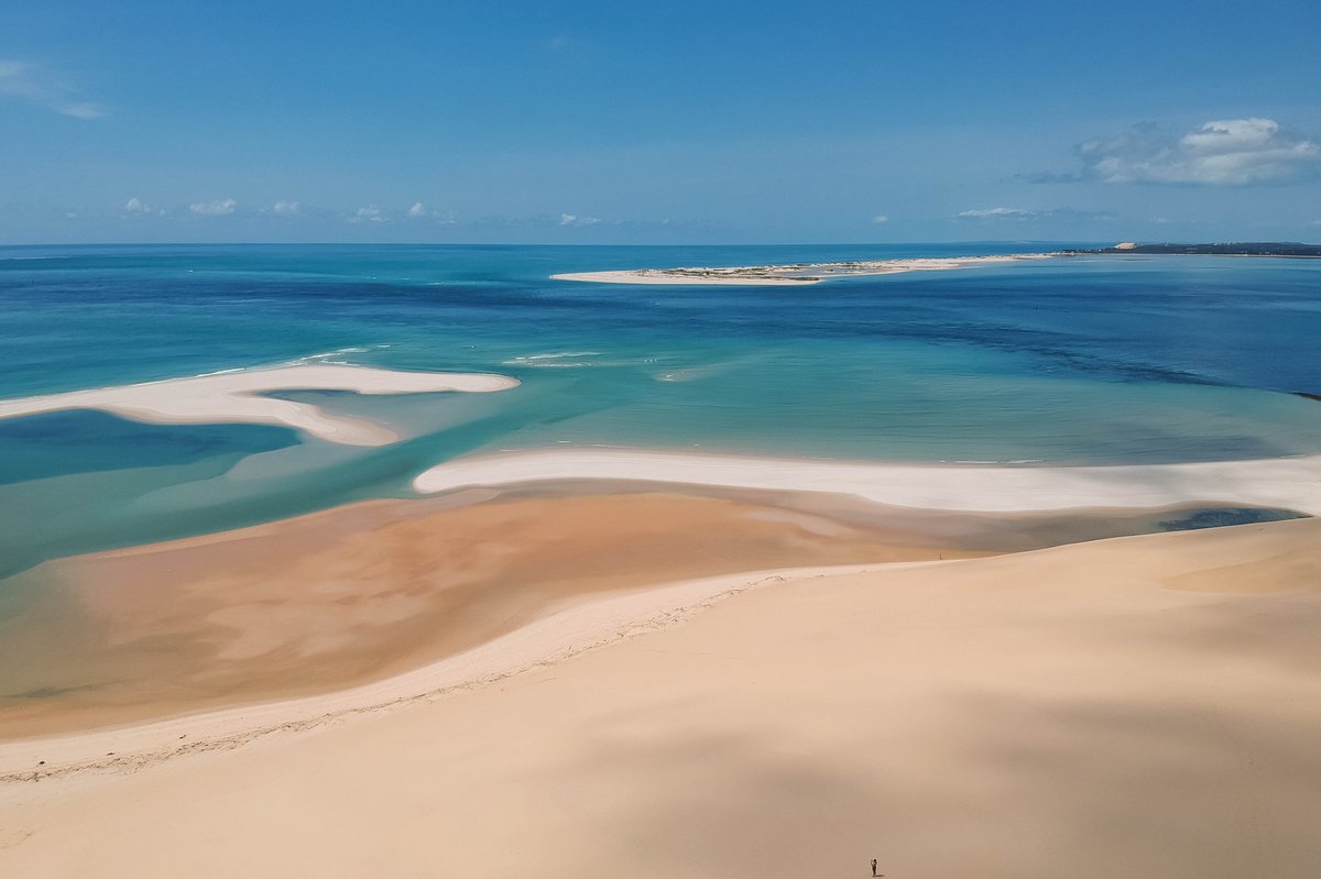 Sanddünen und flache Sandbänke vor einer ruhigen Meeresküste unter blauem Himmel