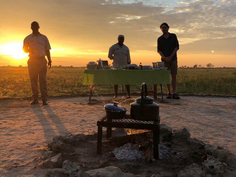 3 Personen bei Sonnenuntergang mit Buffet und Kessel auf offenem Feuer