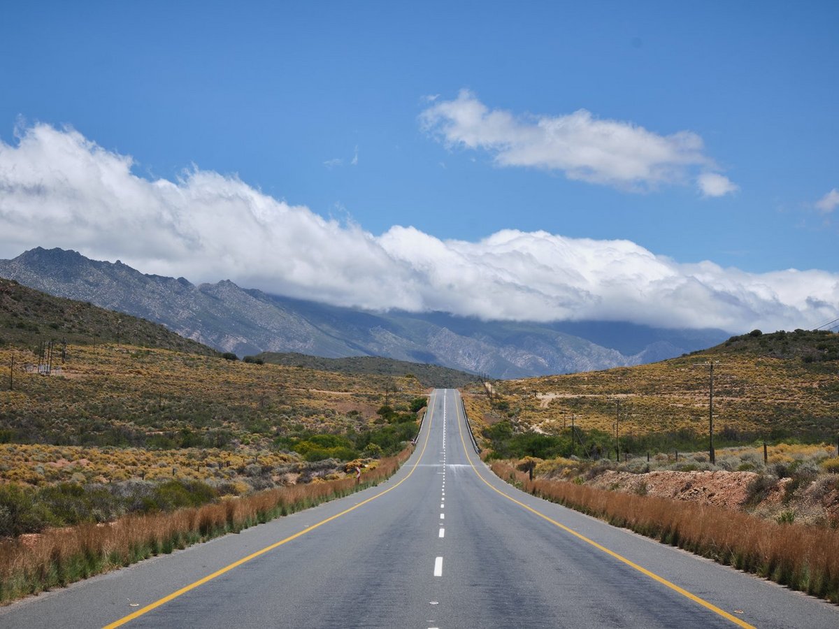 Strasse führt durch trockene Landschaft auf Berge und blauen Himmel zu