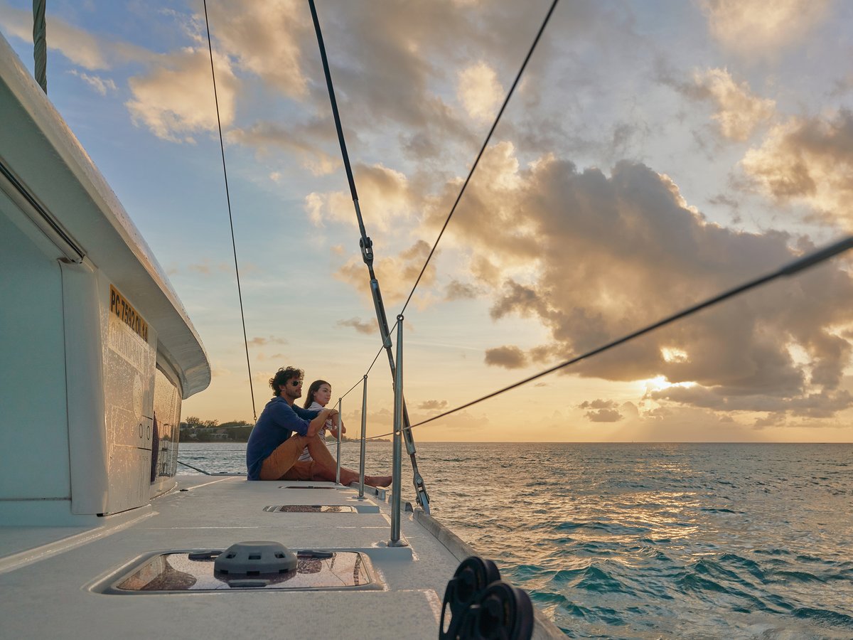 Zwei Personen sitzen auf dem Deck eines Segelbootes und blicken auf das Meer bei Sonnenuntergang