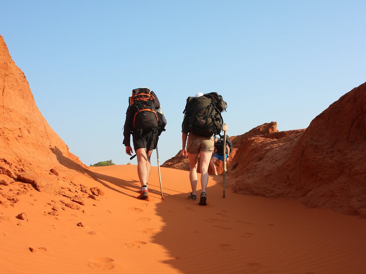 Zwei Wanderer von hinten laufen durch rote Sandberge