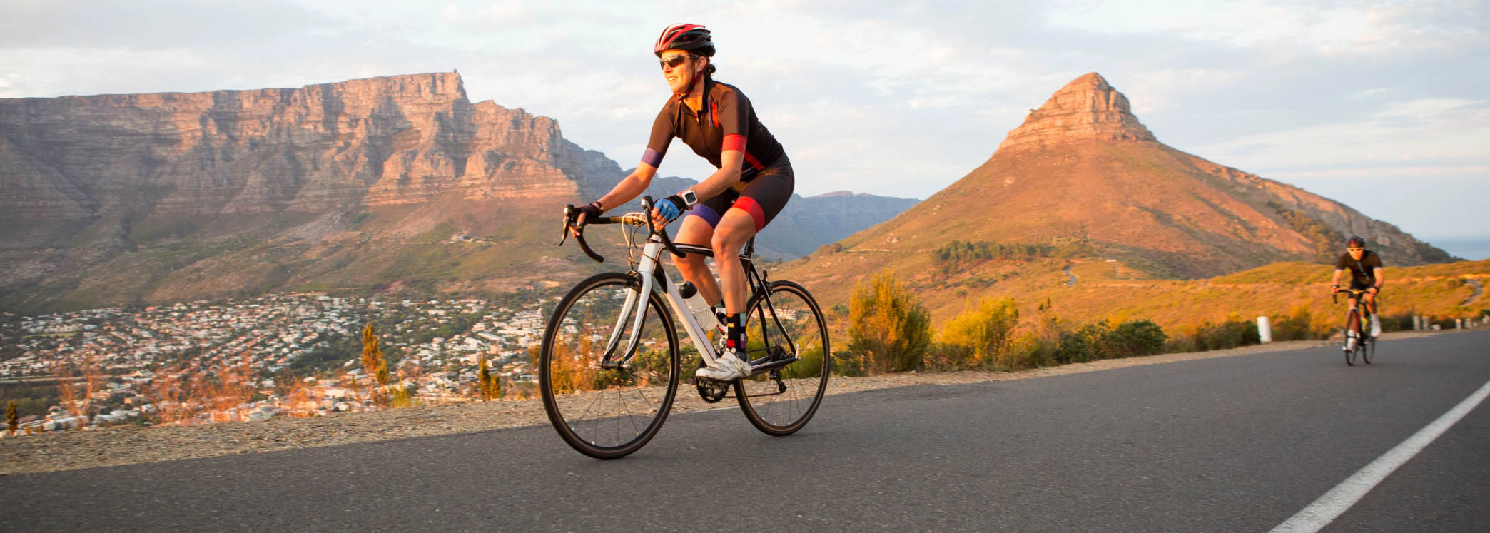 Radfahrer fährt auf einer Straße vor einer Berglandschaft mit Tafelberg im Hintergrund